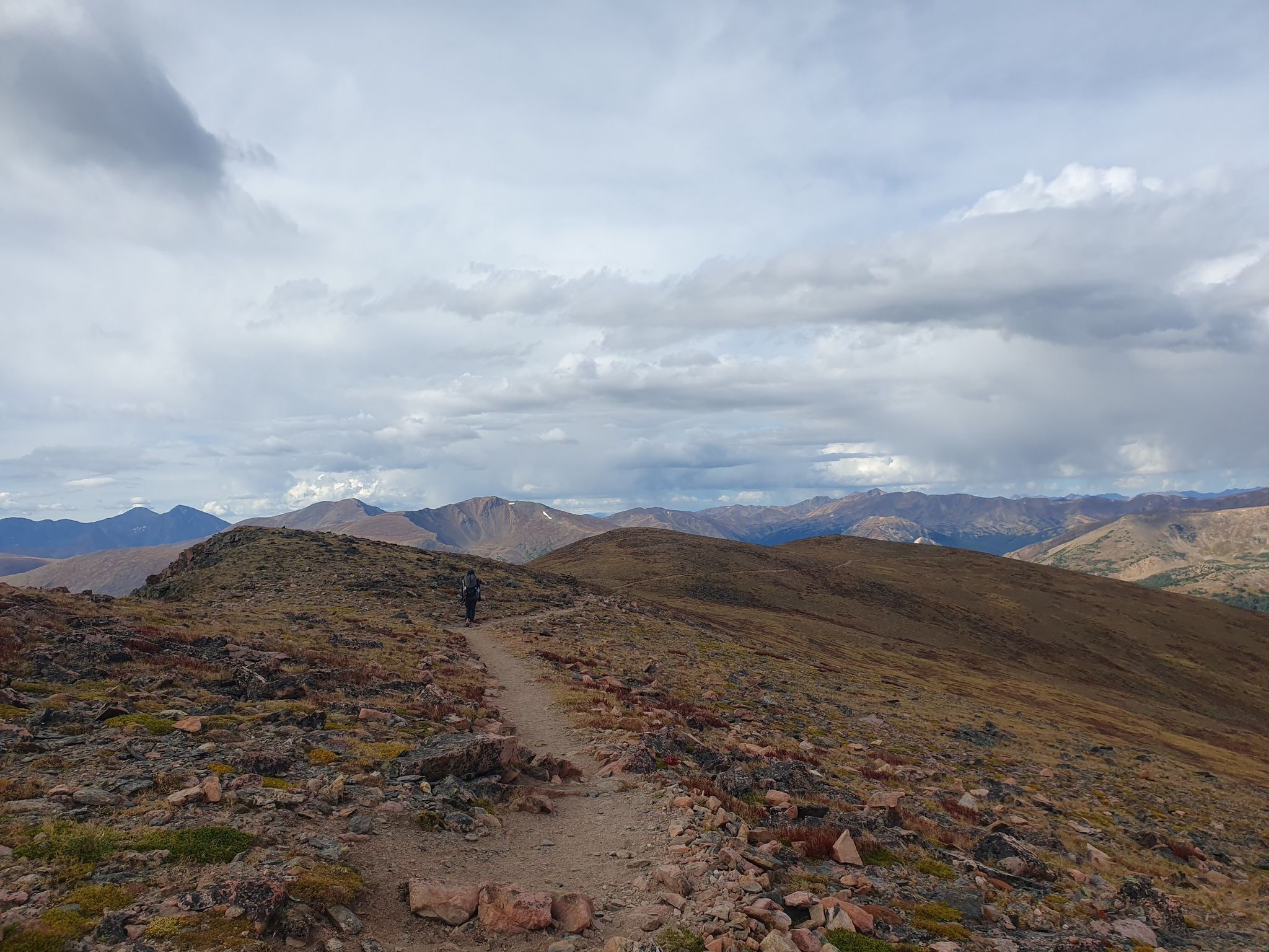 A hiker on a rocky mountain ridge under a cloudy sky. - Mount Flora Trail