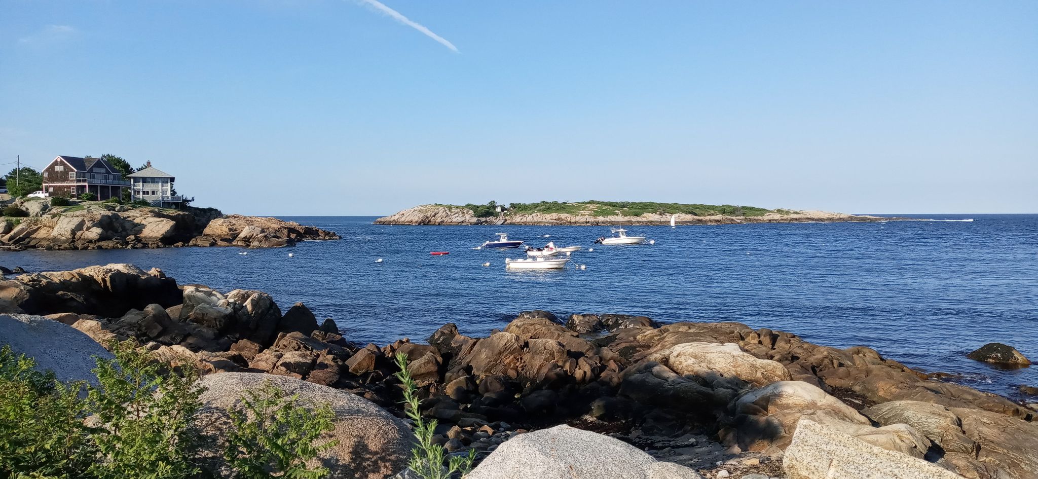 Sunny rocky shore overlooking a bay with boats and a distant island. - Halibut Point State Park – Rockport Harbor loop from Halibut Point State Park