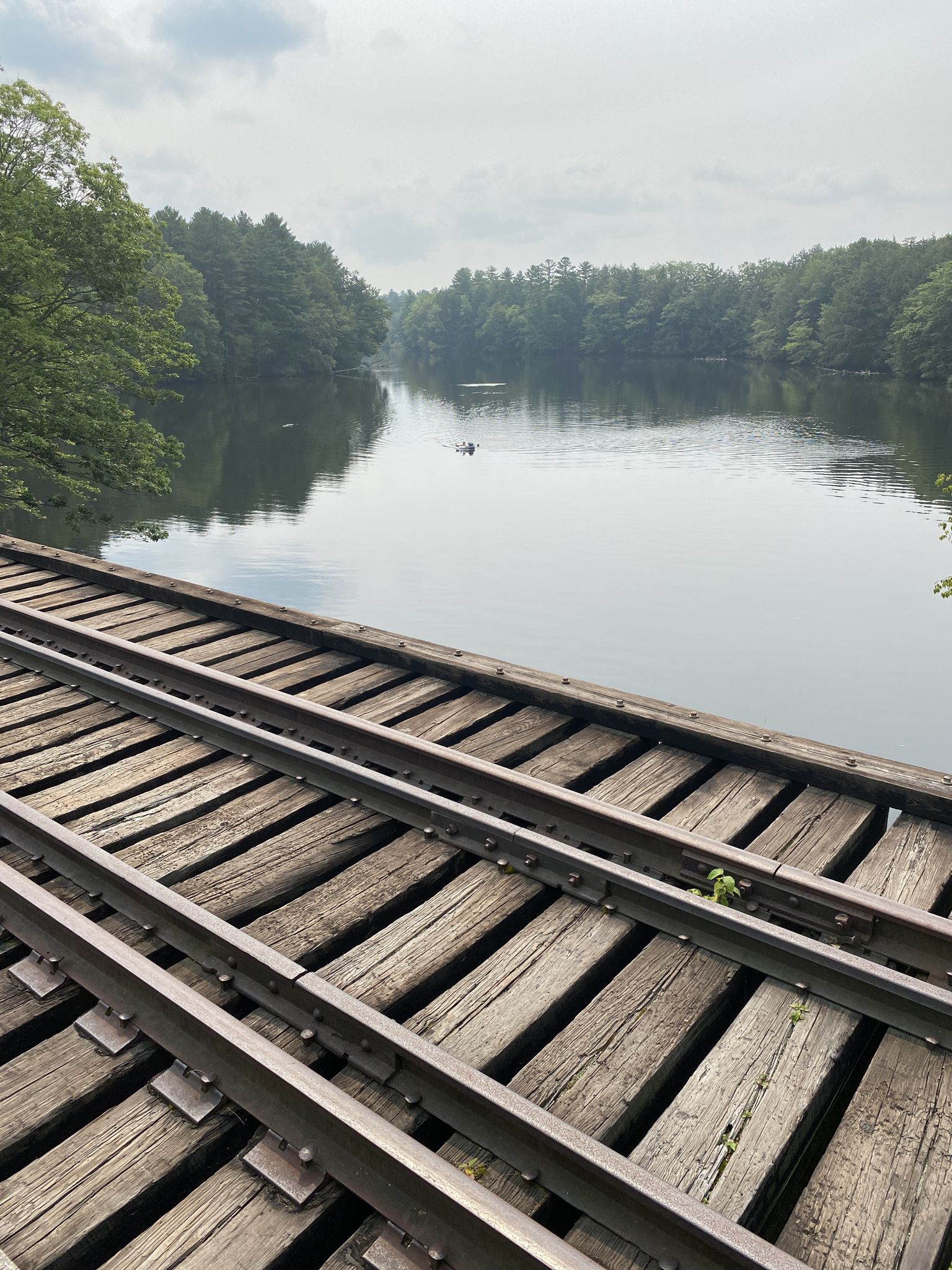 Wooden railroad tracks cross over a calm lake surrounded by green trees. - Snake Pond – Mountain Division Trail loop from Little Falls