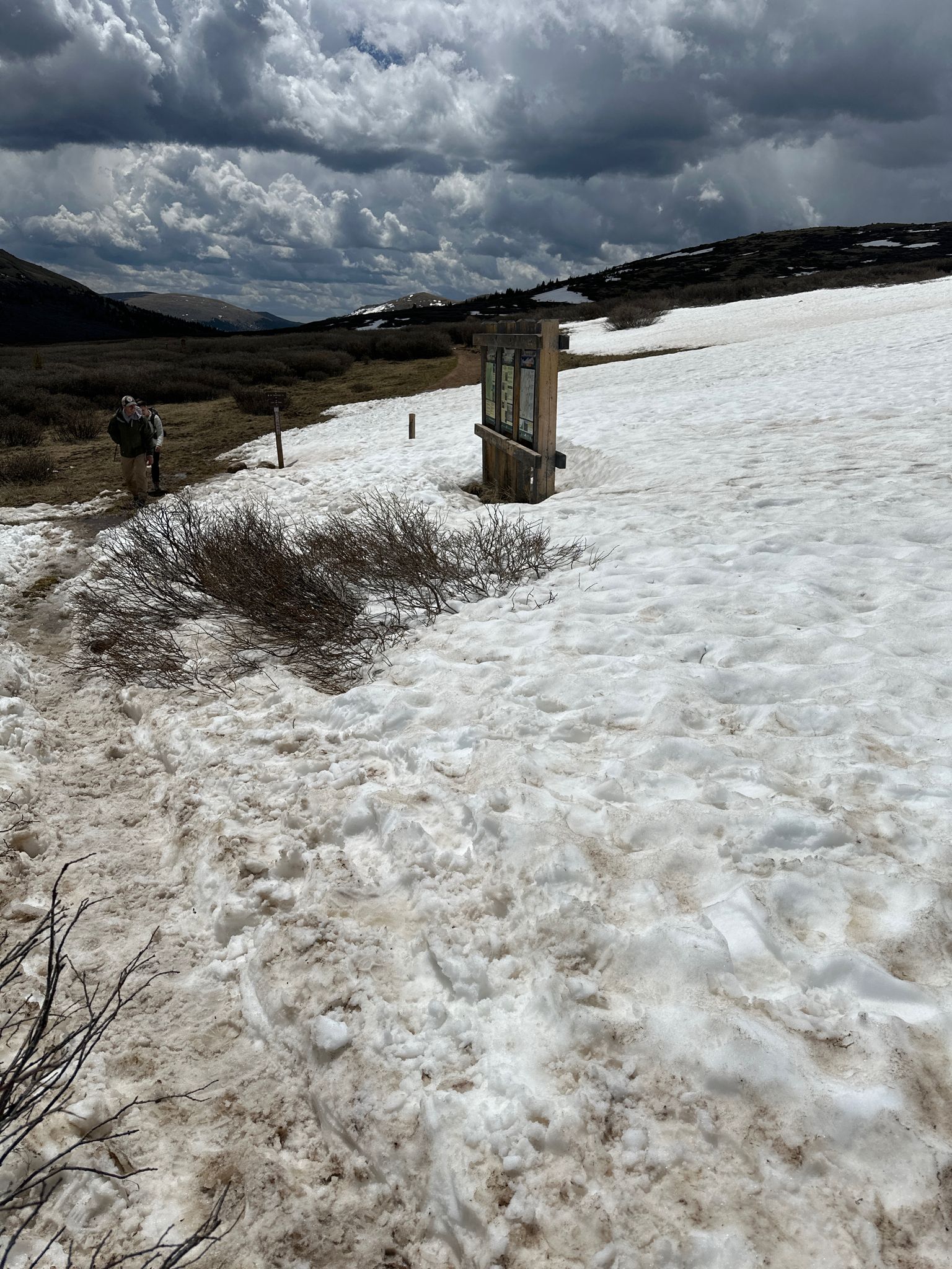 Person walks on a snowy trail with dark clouds overhead and distant mountains. - South Park 600 to Square Top Lakes