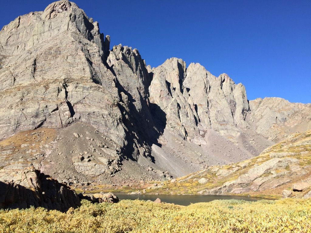 Rugged mountains overlook a small lake and golden alpine grass on a clear day. - Humboldt Peak Trail