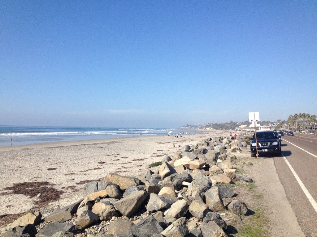 Sunny beach with calm ocean, coastal road, and rock barrier. - Cardiff State Beach – San Elijo Lagoon Estuary Canal loop from Solana Beach