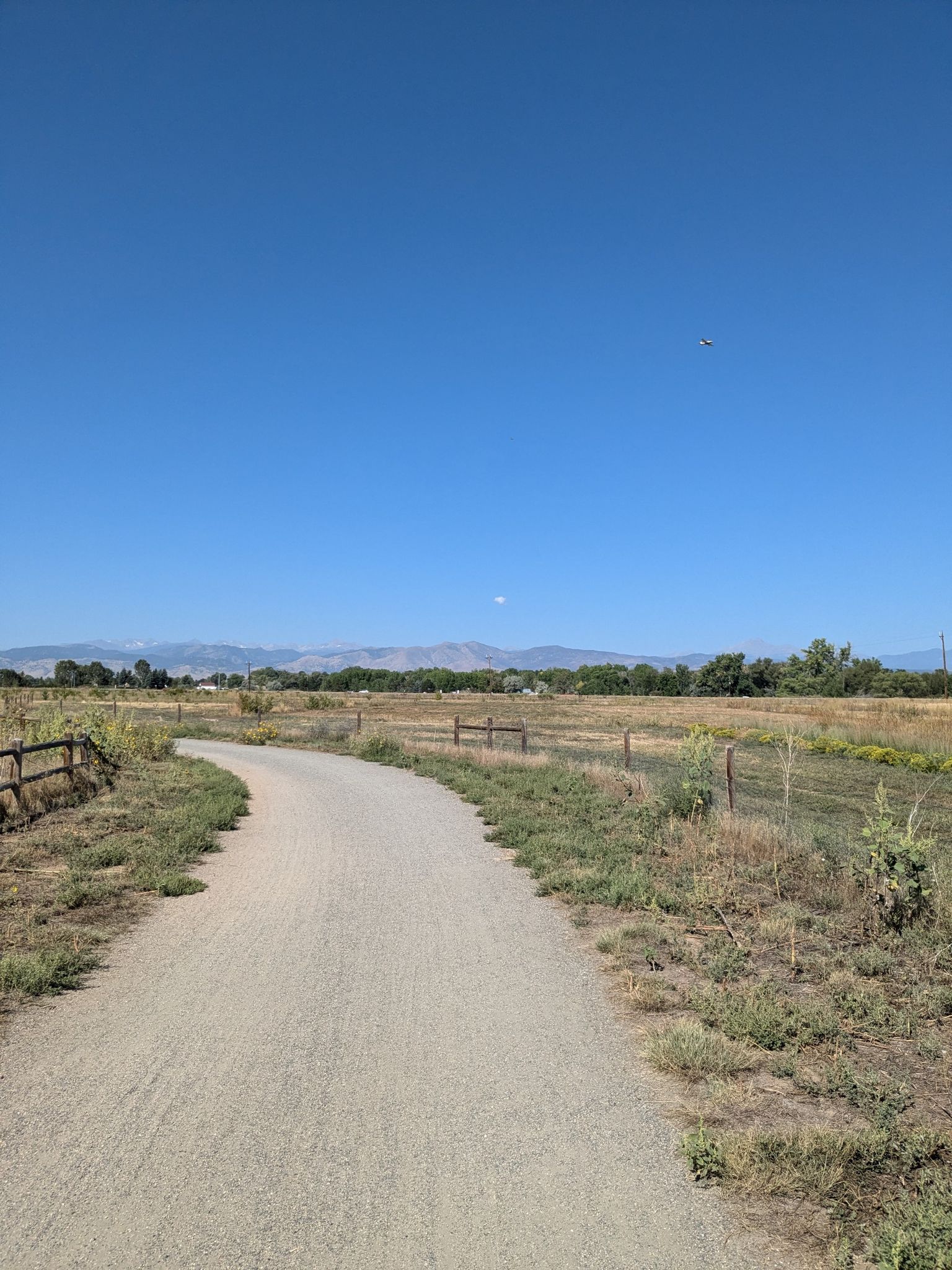 Gravel path through dry fields, distant mountains, clear blue sky. - LoBo Trail – Left Hand Creek Park loop from Niwot