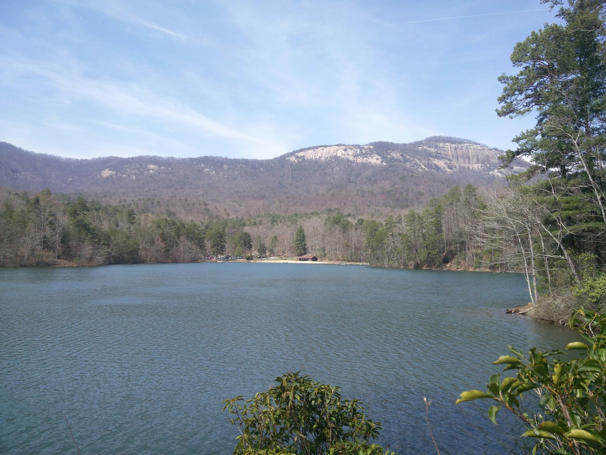 Wide blue lake surrounded by forested mountains under a bright, clear sky. - Lakeside Trail