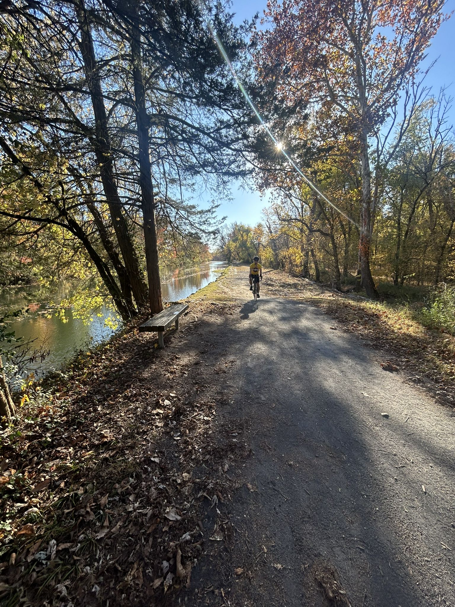 A person cycles on a sunny dirt path beside a canal in autumn. - Challenging Downhill Twist – Red Trail loop from Rocky Hill
