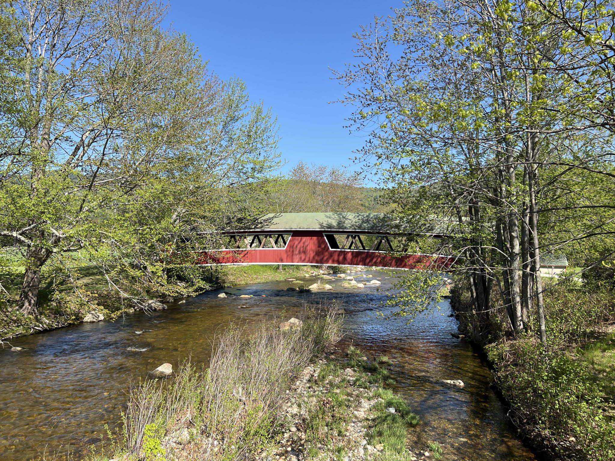 Red covered bridge spanning a clear river, surrounded by lush green trees. - Jackson Falls loop — Gravel