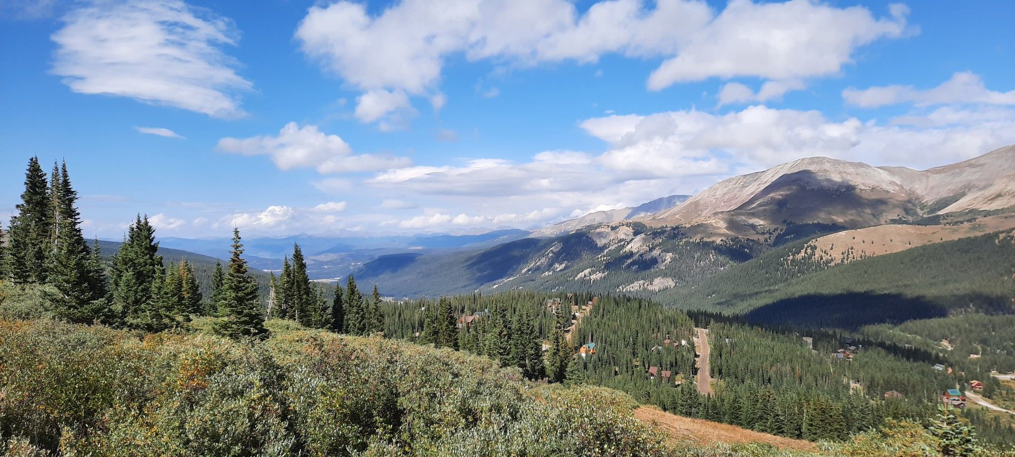 Panoramic view of a vast mountain landscape under a bright, cloudy sky. - North Star Mountain Summit