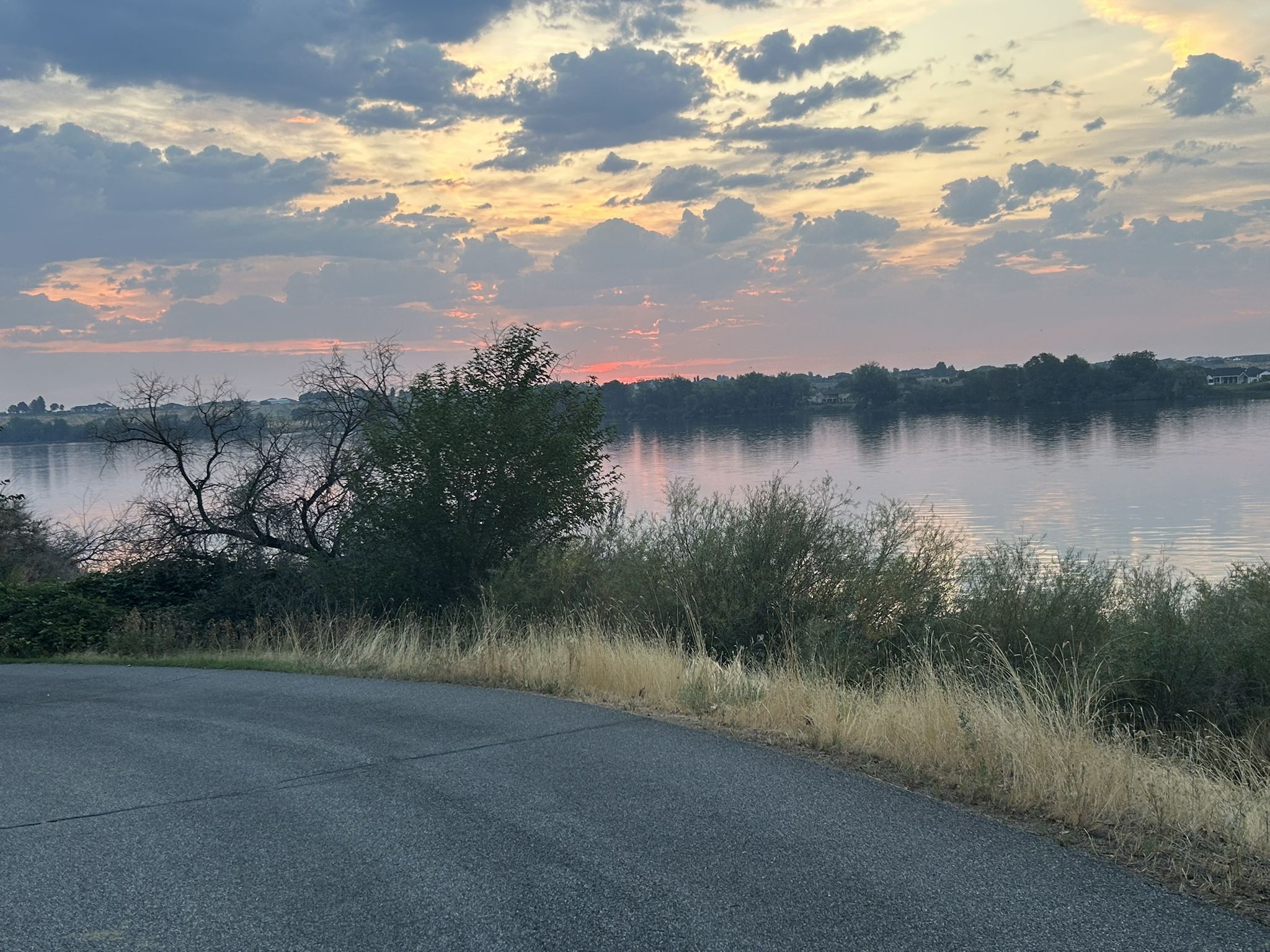 A vibrant sunset over a calm river, with a road and trees. - Yakima Delta – Chamna Natural Preserve loop from Island View