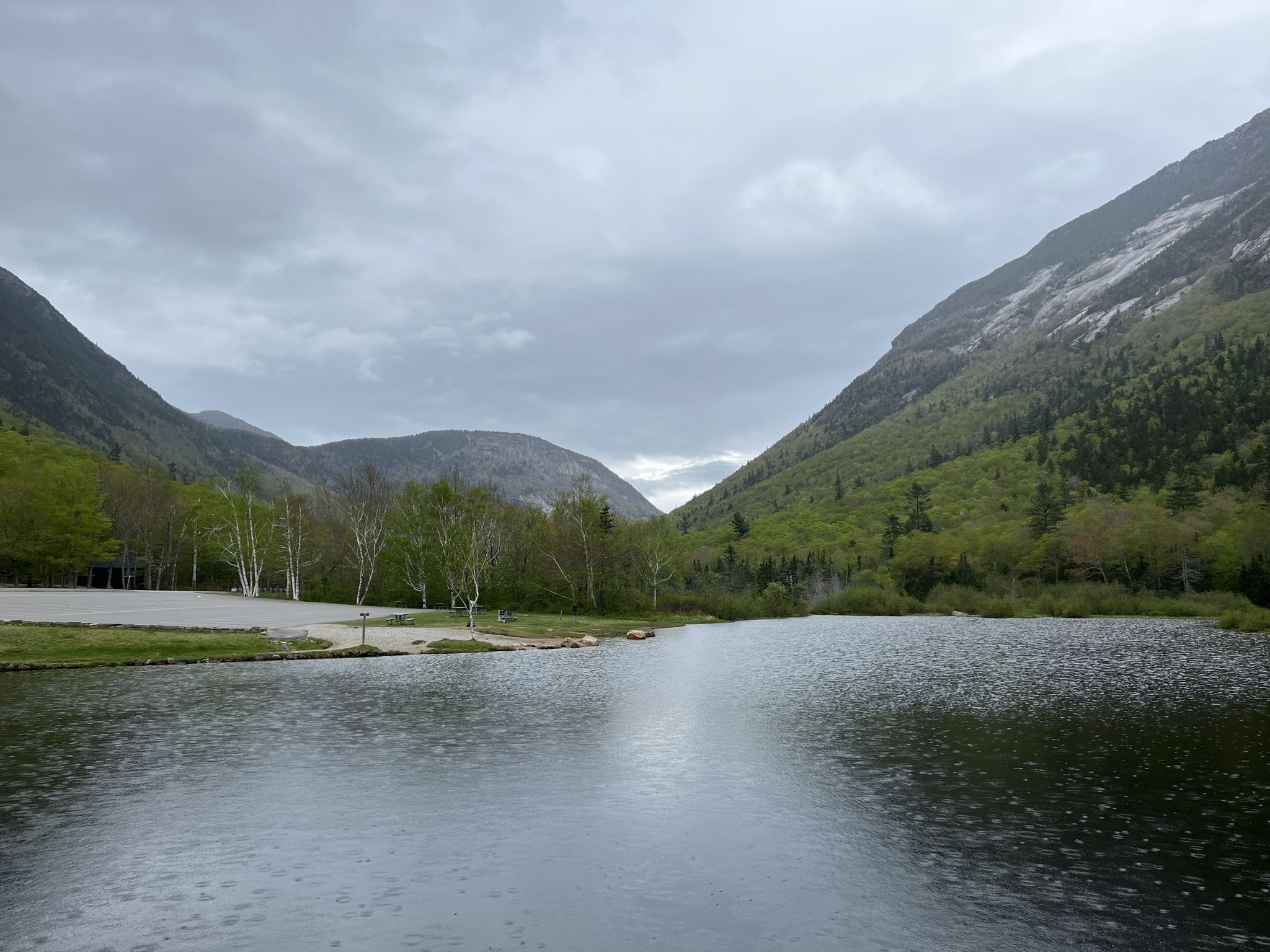 Overcast day with raindrops on a lake surrounded by green mountains and trees. - Arethusa Falls and Frankenstein Cliff Loop