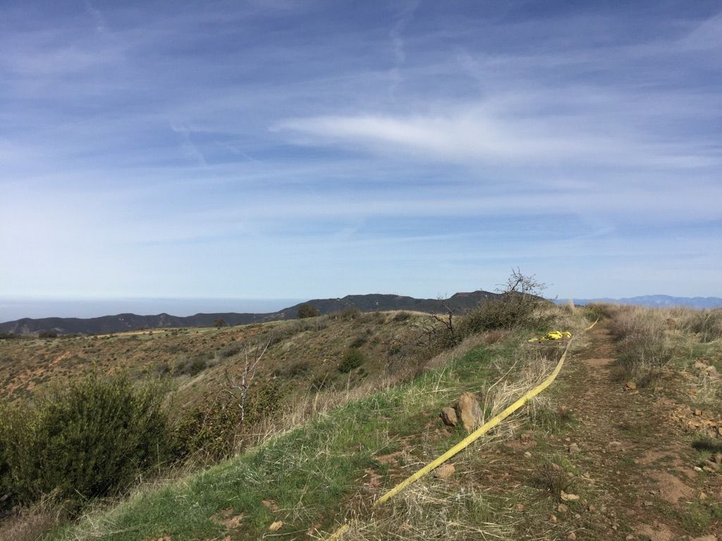 Dirt path with yellow hose on a grassy hillside under a partly cloudy sky. - Silverado Motorway to Bedford Peak