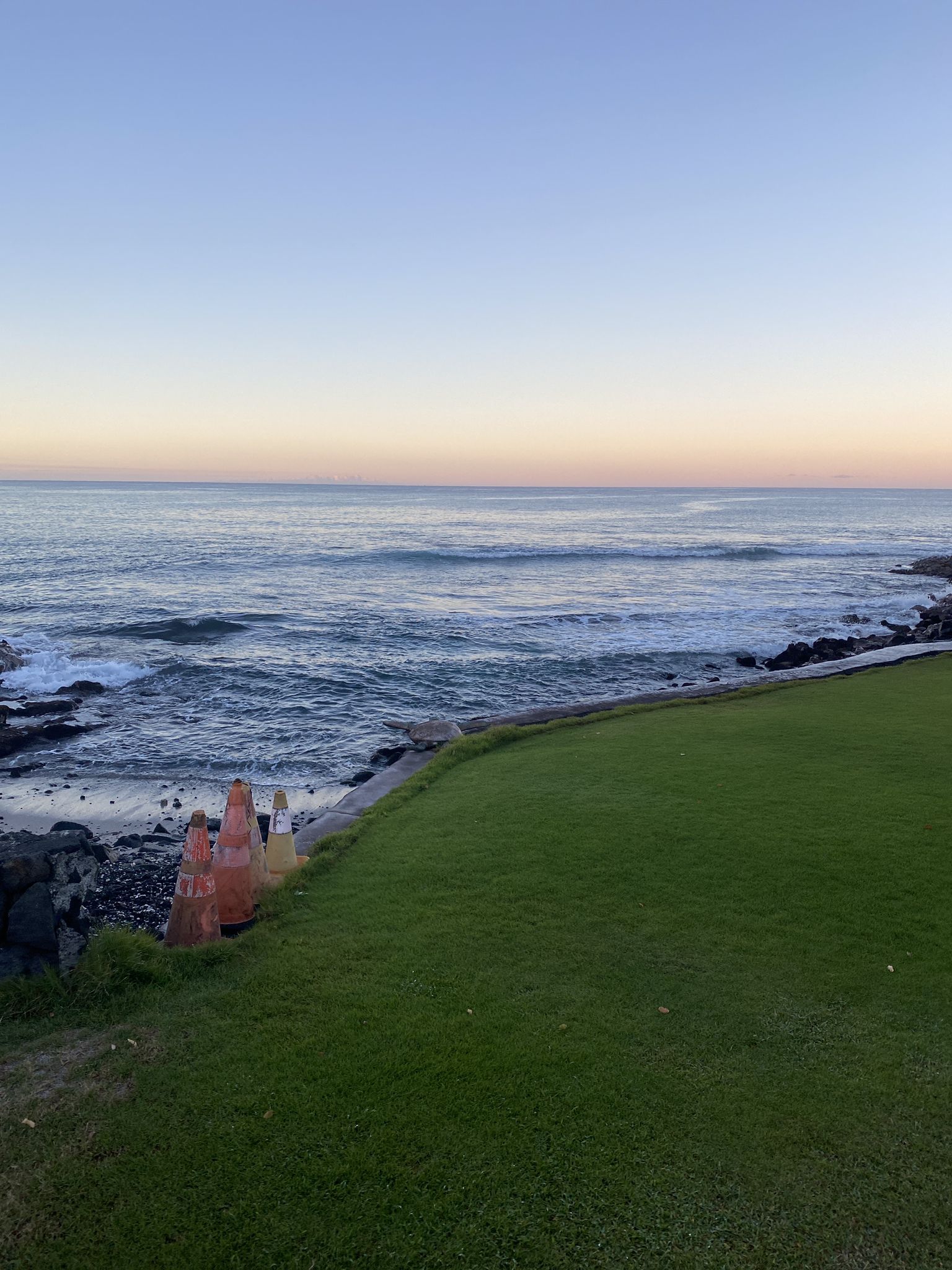 Gentle ocean waves meet a grassy shore under a soft pastel sky. - White Sands Beach Park loop from Sea View