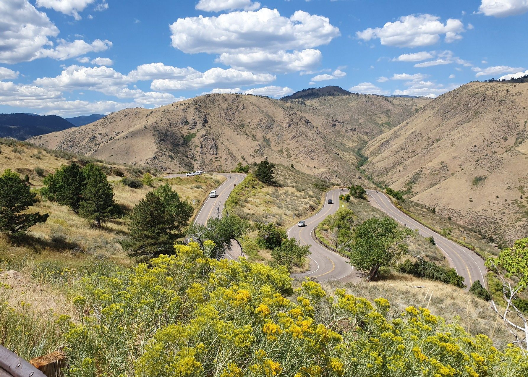 Winding road through arid mountains under a bright, partly cloudy sky with cars. - Colorado Railroad Museum to Lookout Mountain Nature Preserve