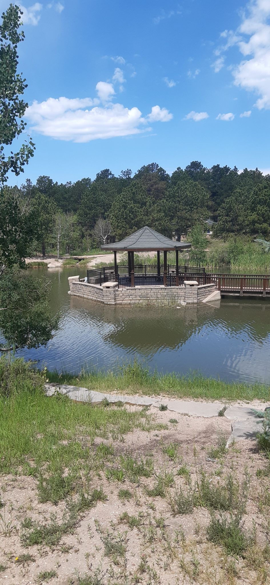 Gazebo on a lake with a wooden bridge, surrounded by green trees. - Fox Run Loop Trail