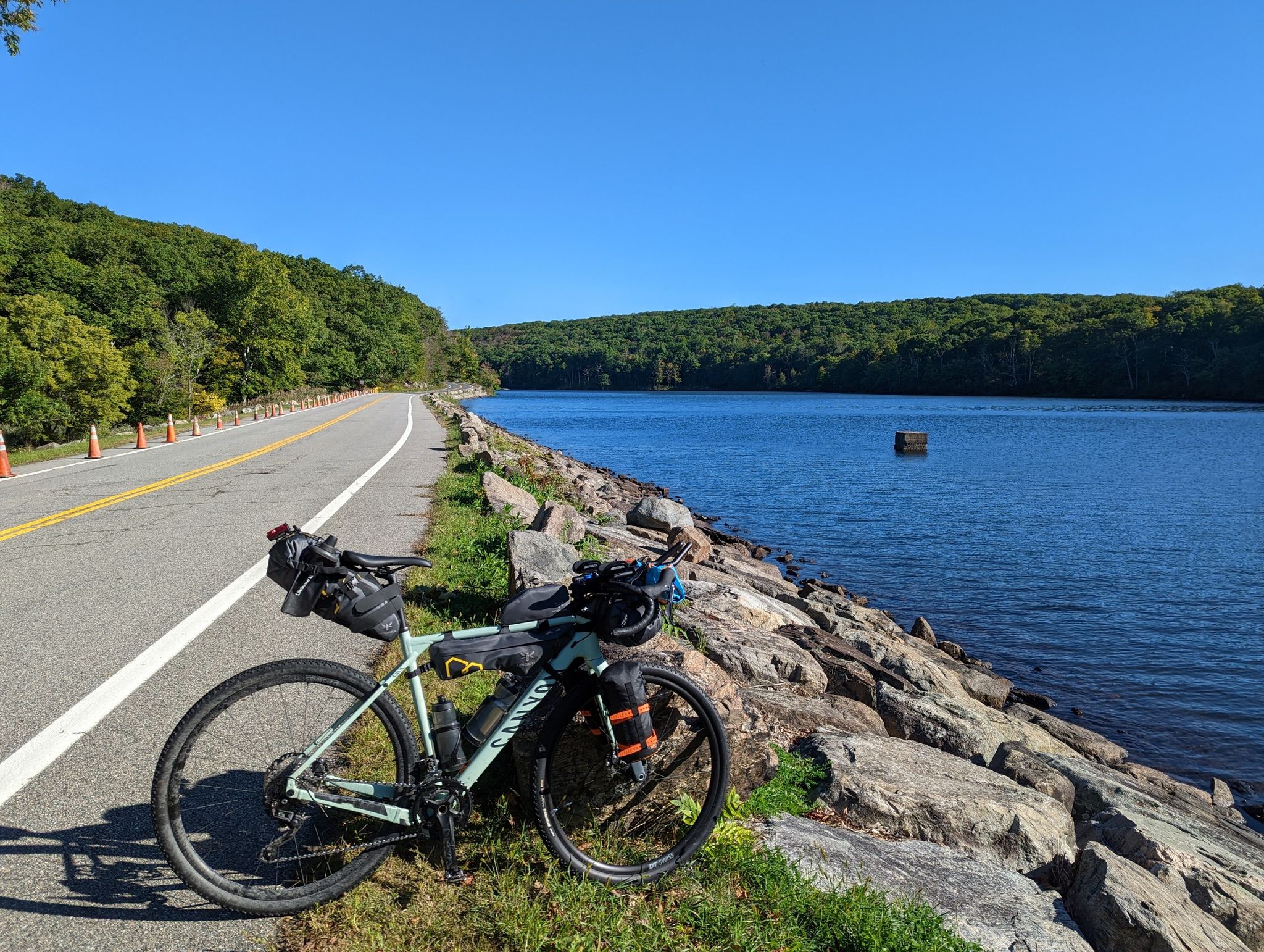 Bicycle parked on a rocky shore next to a road and a blue lake. - Lake Tiorati – Lake Tiorati East Side loop from Fingerboard Mountain