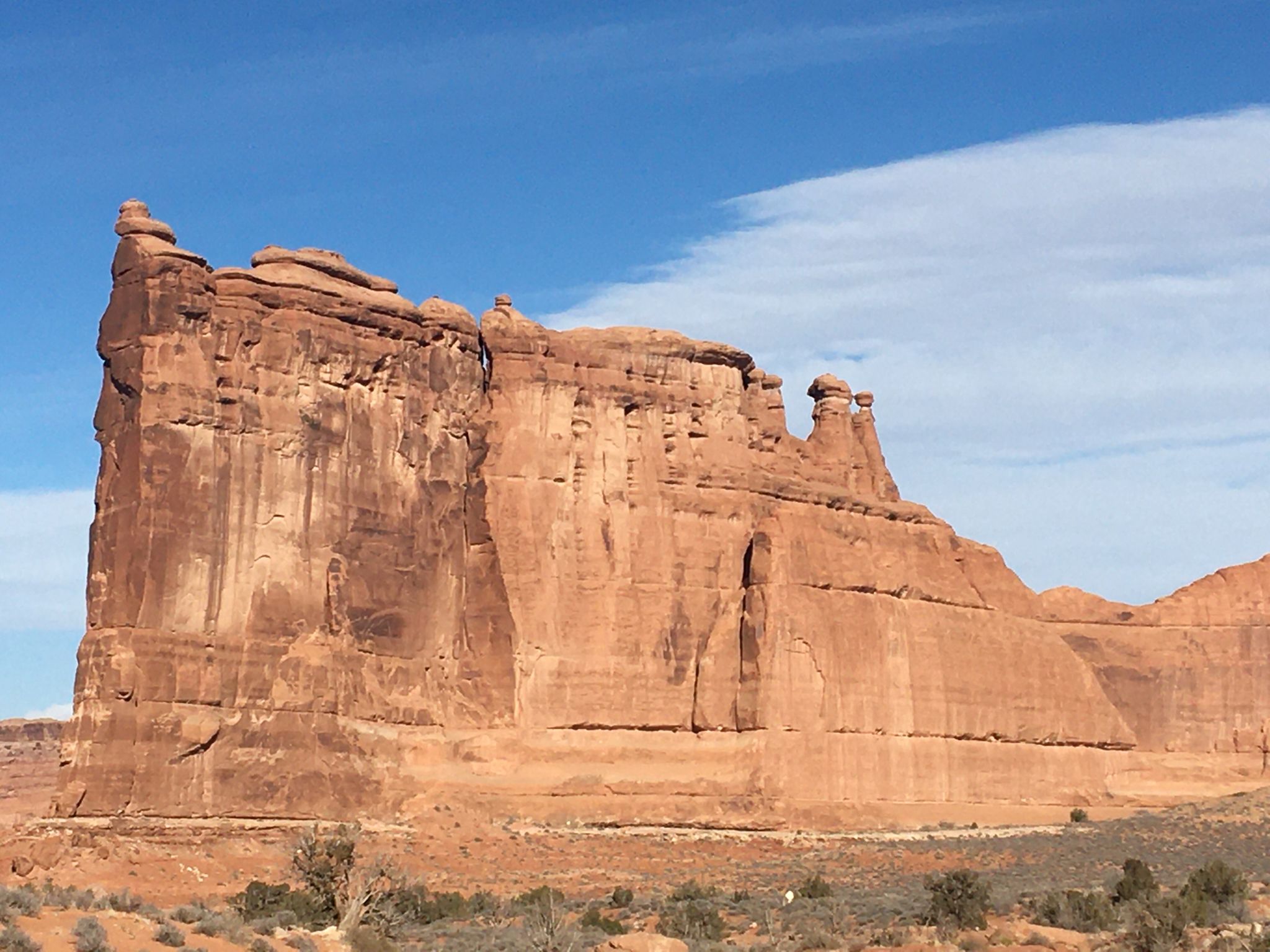 Massive red rock wall with smaller formations under a partly cloudy sky. - Park Avenue Trail