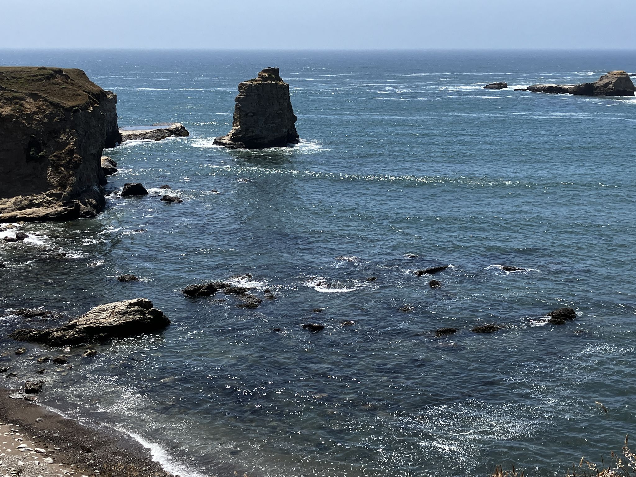 A large sea stack rises from the dark ocean near a rocky coastline. - View to Point Arena Lighthouse loop from Point Arena Lighthouse