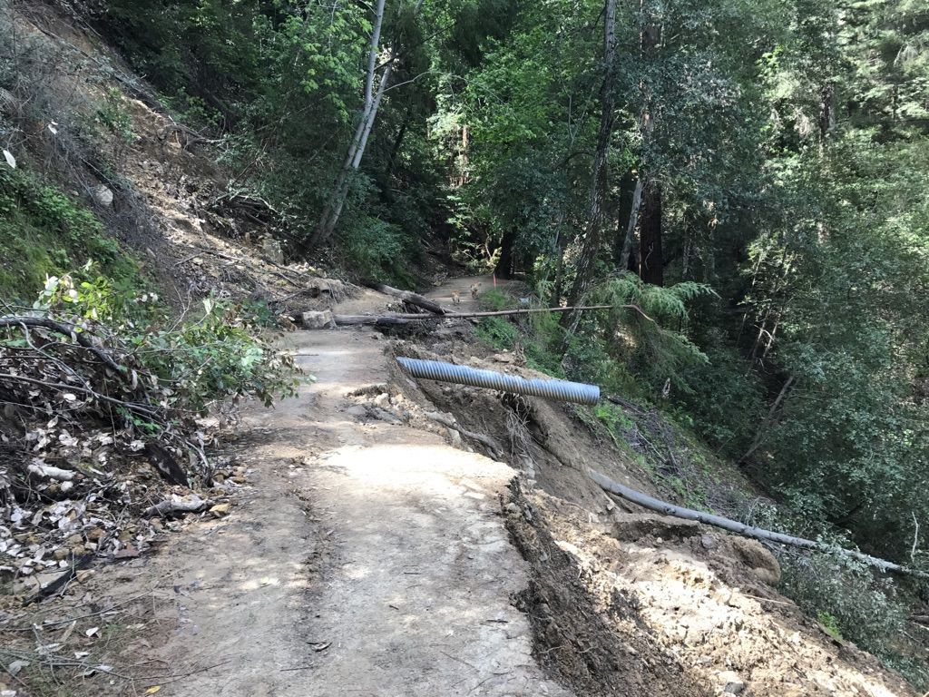 Damaged dirt path on a steep hillside with a large culvert pipe and debris. - John Nicholas Trail to Lake Ranch Reservoir