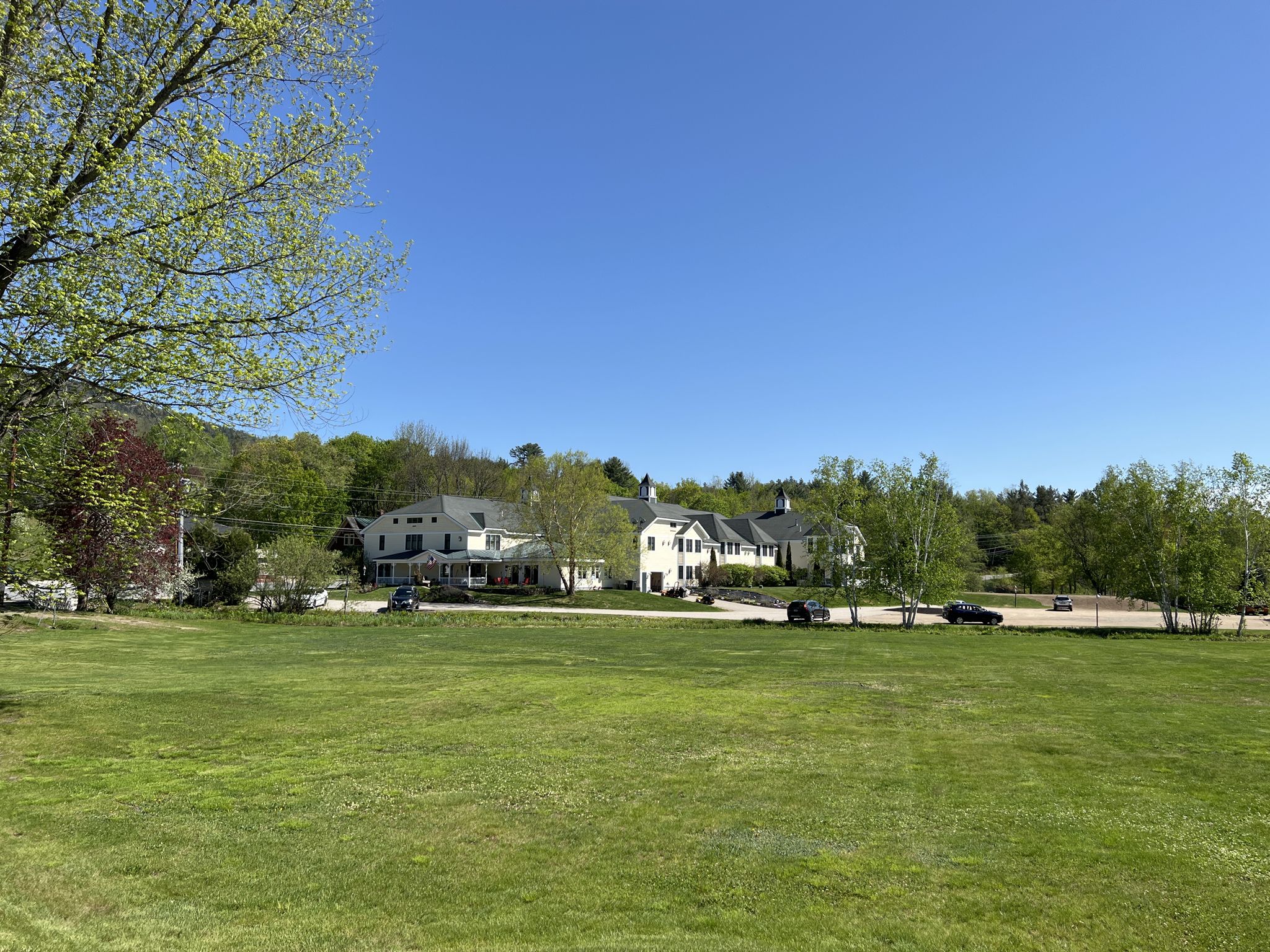 A wide green field in front of large houses and distant hills. - Jackson Falls & Middle Mountain loop