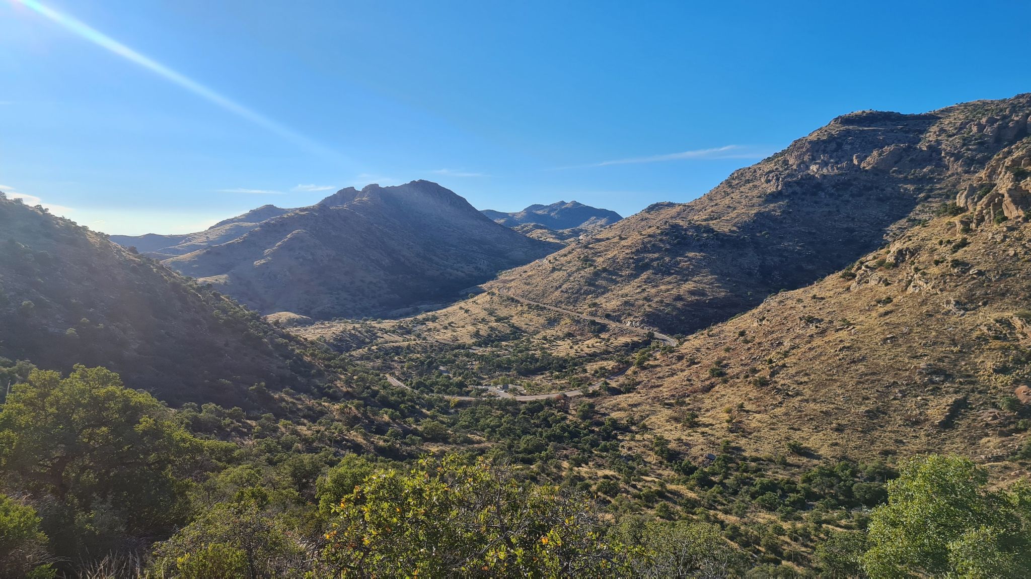 Sunny mountain valley with a winding road and arid vegetation under blue sky. - Bellota Trail