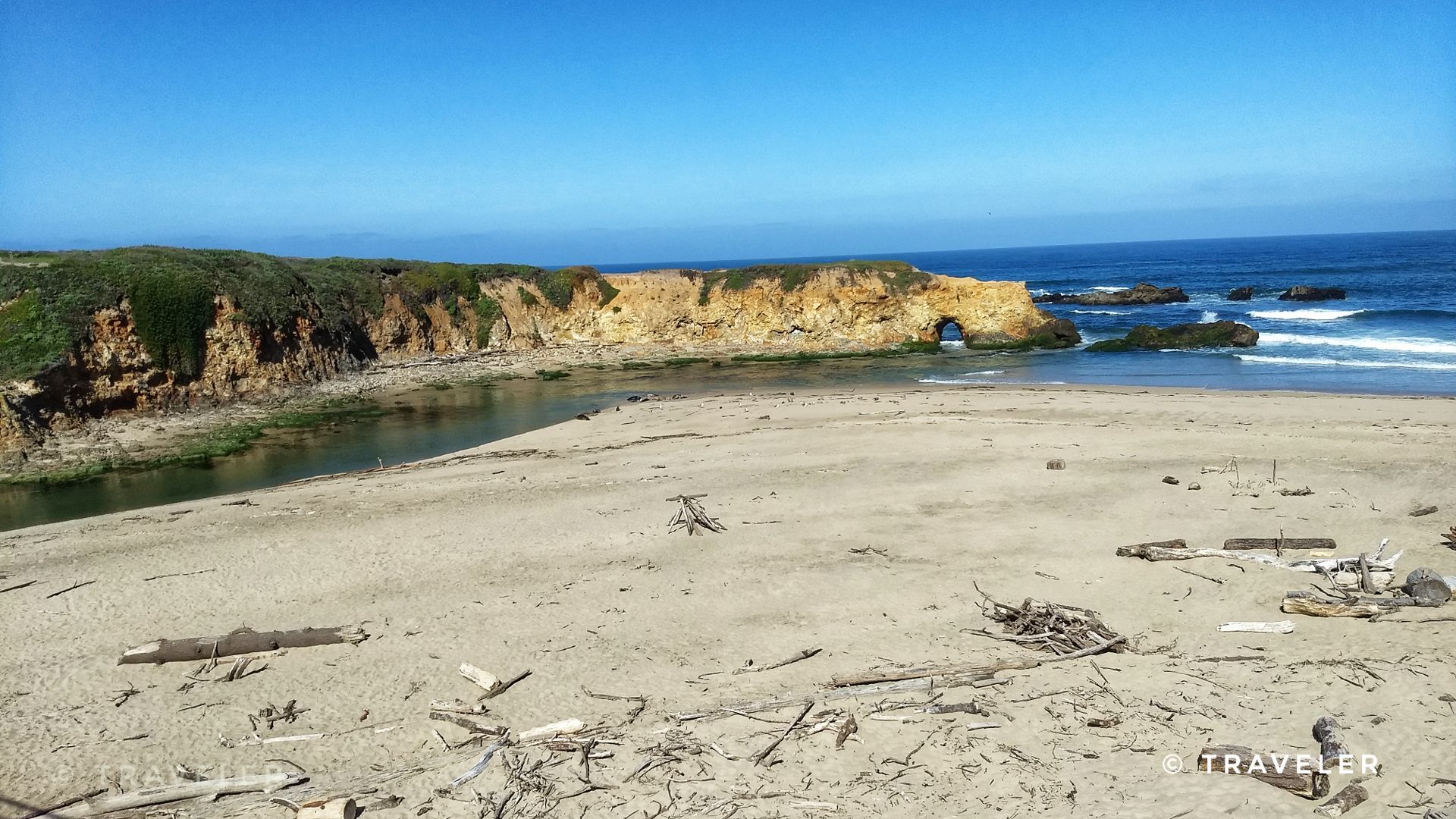 Sandy beach with driftwood, ocean waves, and a rocky sea arch. - Pescadero Creek Road Loop