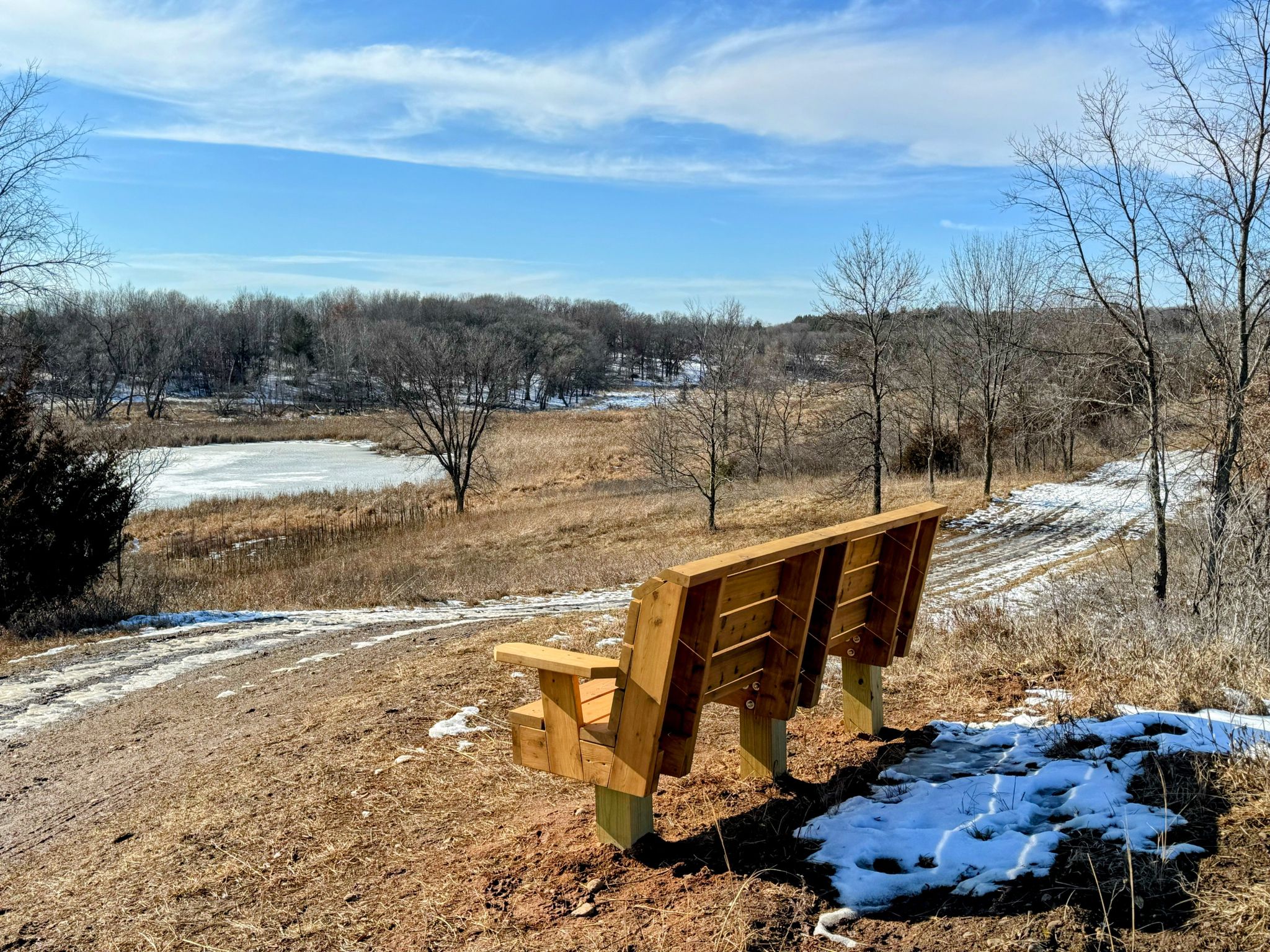 Wooden bench overlooking a snowy field and frozen pond under a blue sky. - Eagle Point Trail