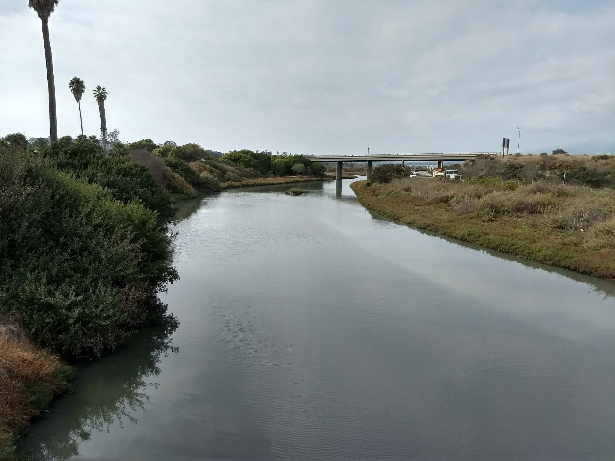 A wide river flows under a distant bridge on an overcast day. - Maria Ygnacio Bike Path and Obern Trail