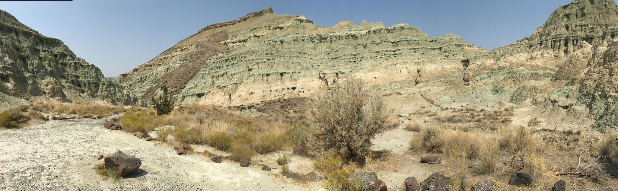 Panoramic view of a wide, arid valley with layered rock formations under clear sky. - Island in Time Trail
