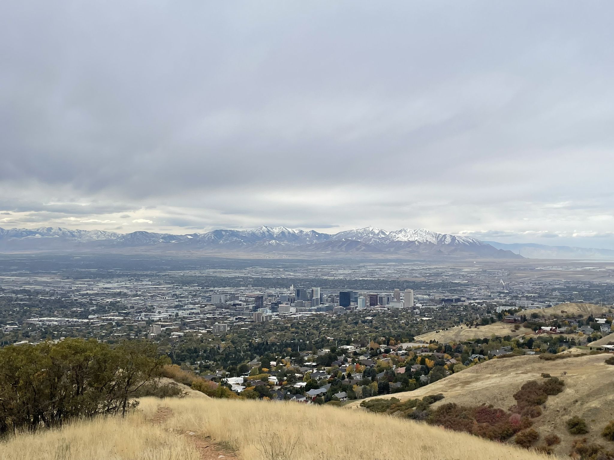 Wide view of a city nestled in a valley with golden hills and snowy mountains. - Bonneville Shoreline Trail, Dry Creek, and Bobsled Loop