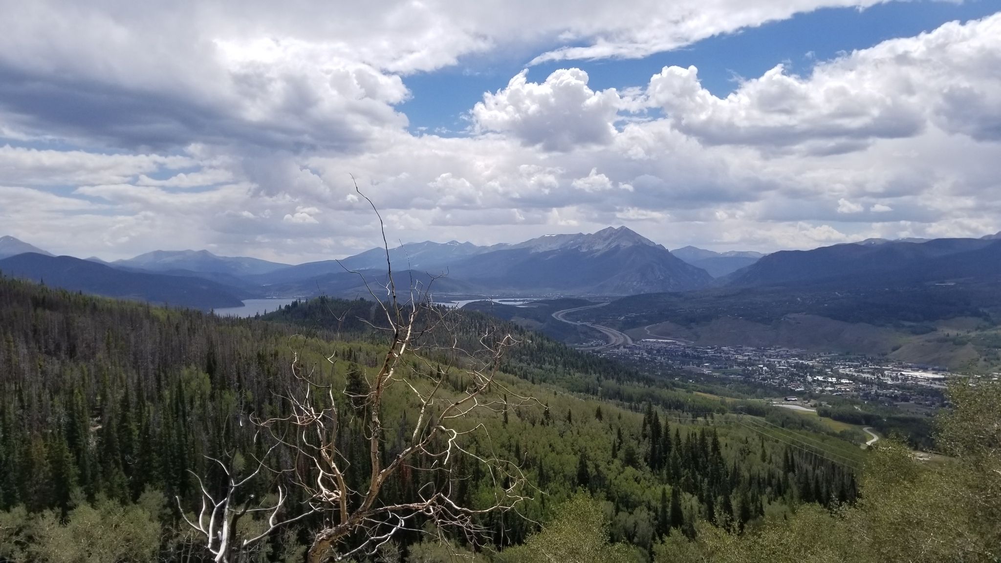 Mountain vista with a lake, town, and diverse forest under a cloudy sky. - Hiking loop from Blue River Ranch Lakes