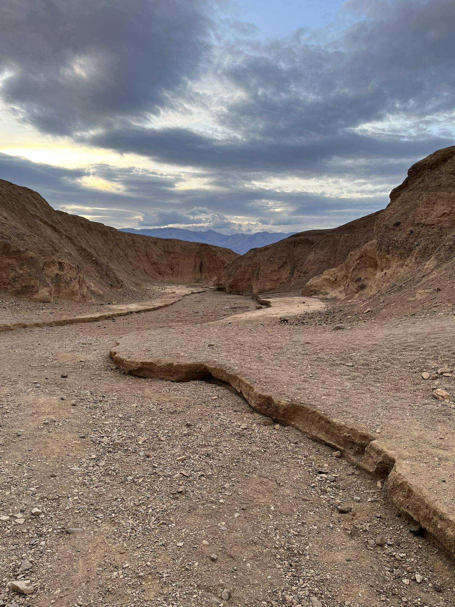 A dry, winding desert wash with steep canyon walls under cloudy skies. - Artists Palette Trail