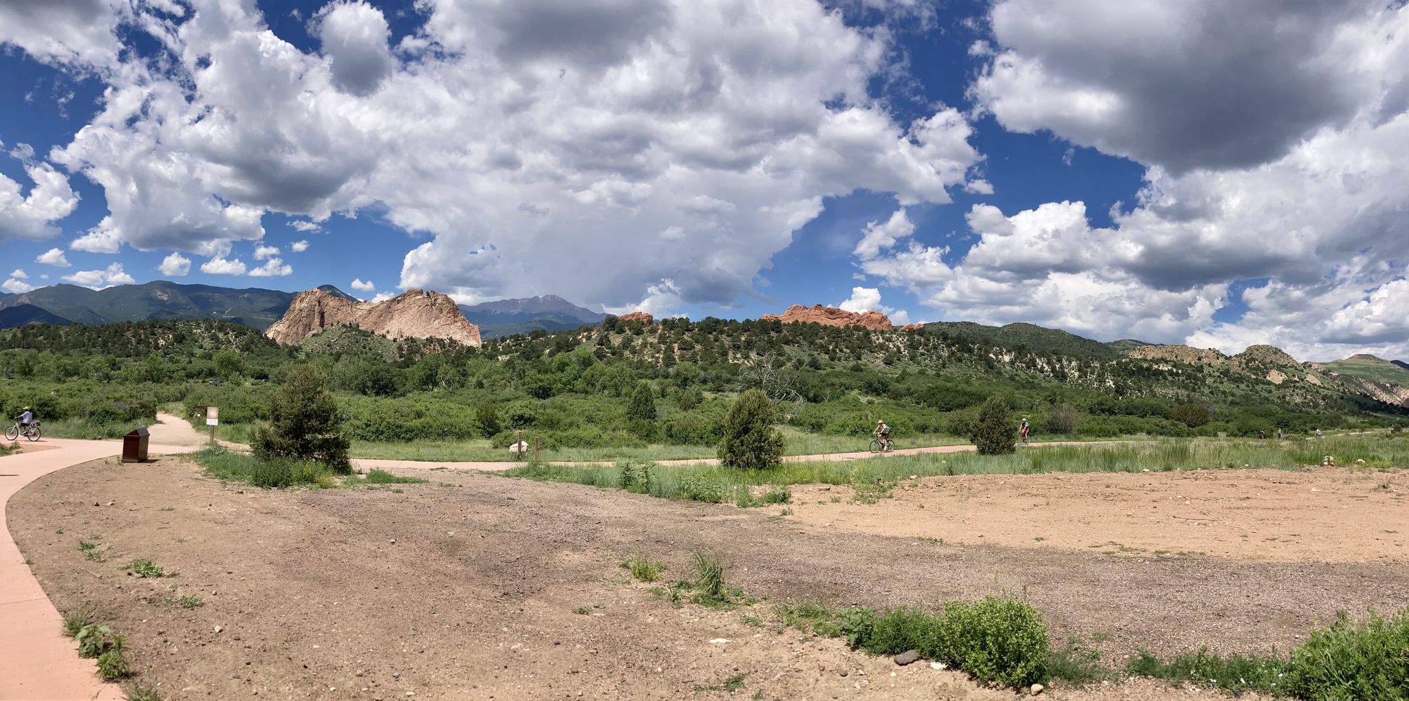 Panoramic view of red rock formations, green hills, and distant cyclists under clouds. - Garden of the Gods Park loop via Blodgett Peak Open Space