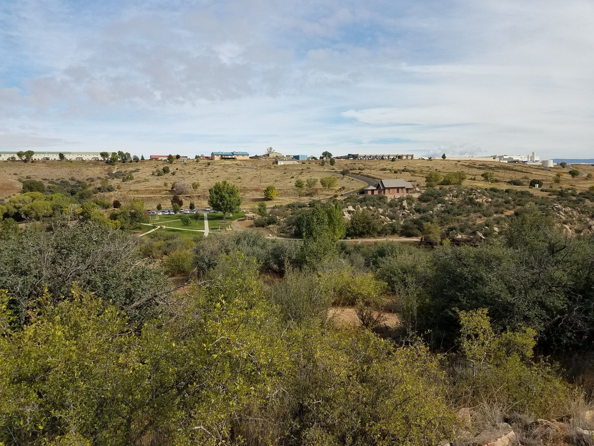 Hilly landscape with green trees, distant buildings, under a cloudy sky. - Lynx Creek Loop