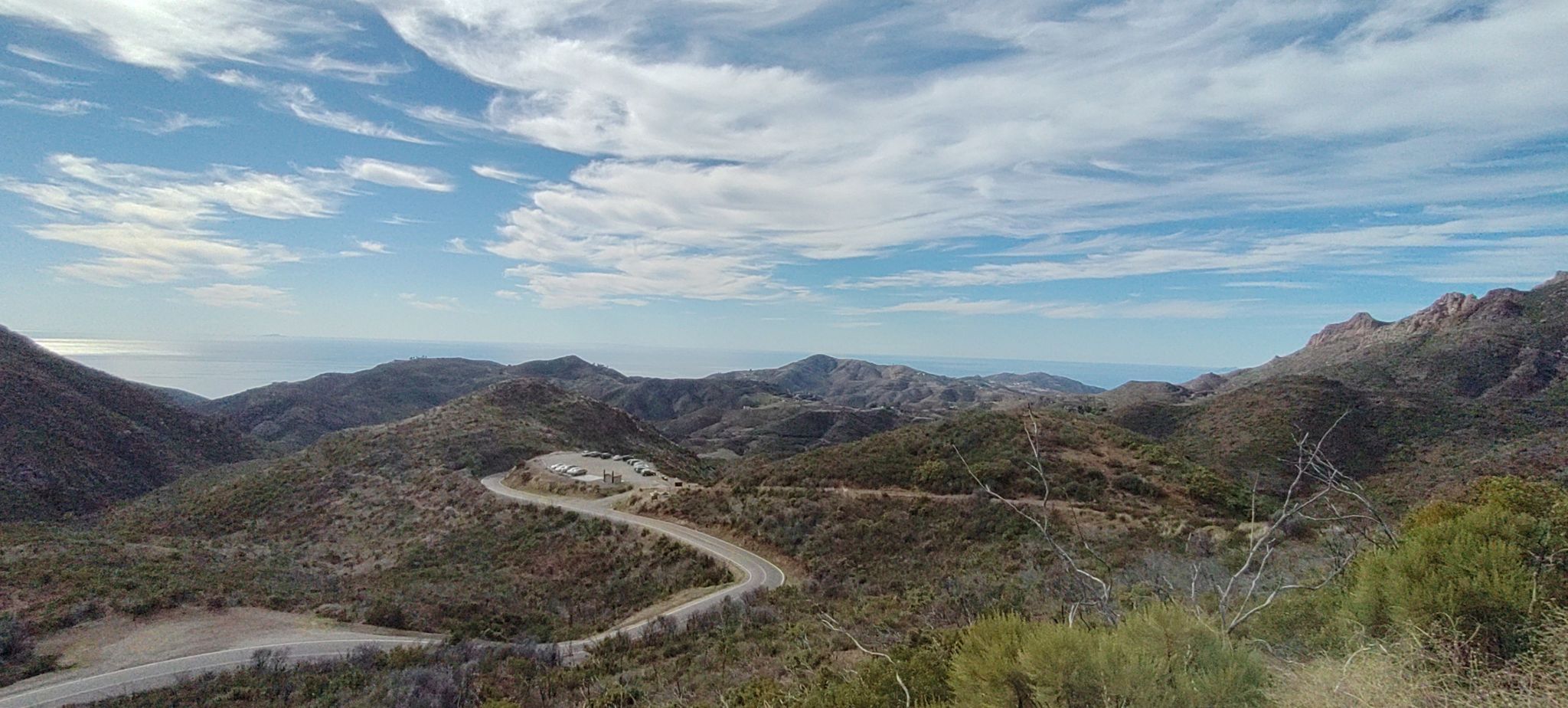 Winding road through dry mountains, with a distant ocean under a blue sky. - Sandstone Peak Trailhead – Split Rock Picnic Area loop from Circle X Ranch