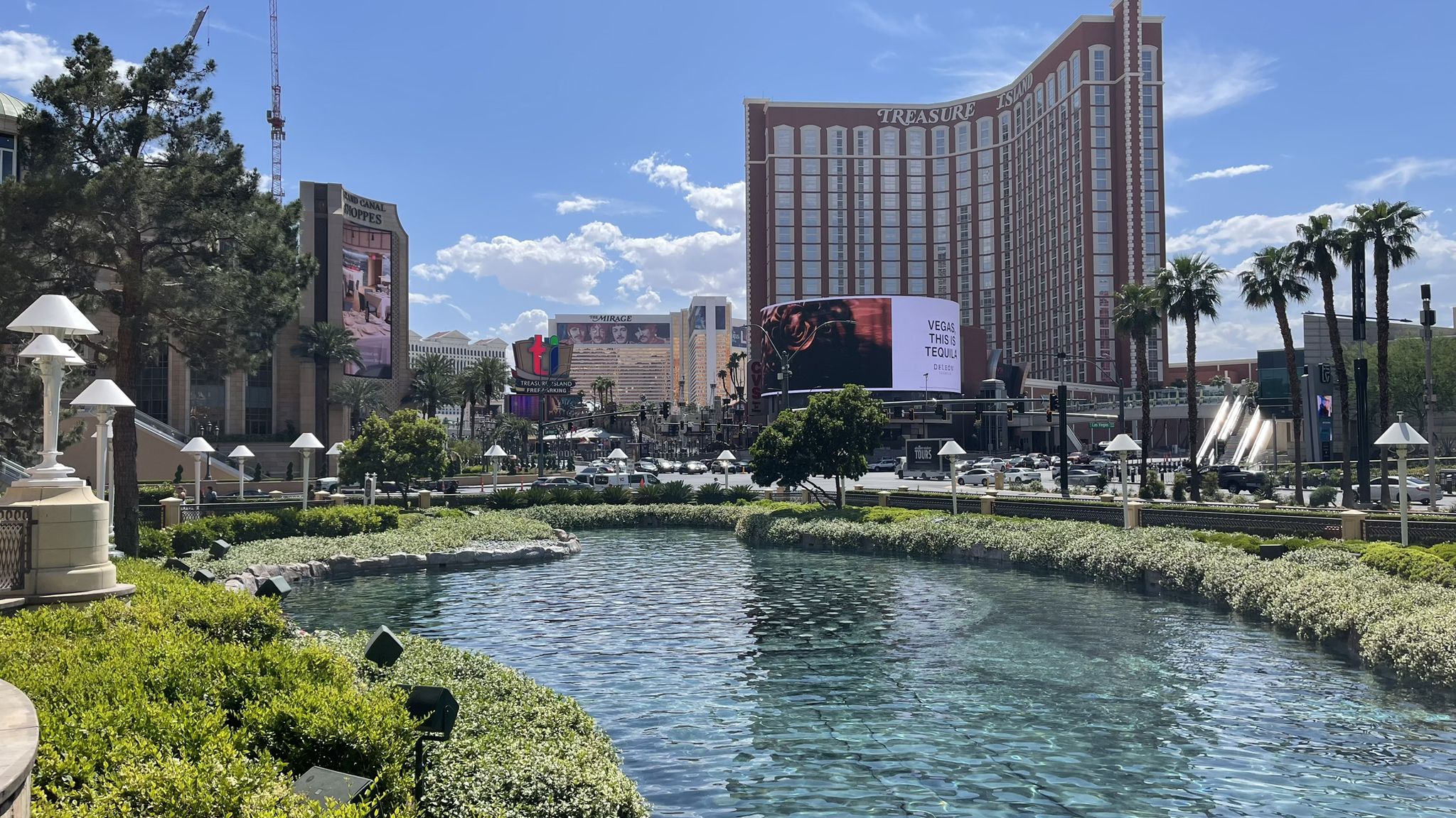 Large buildings overlook a canal with green landscaping under bright daylight. - Fountains of Bellagio – The Venetian Resort loop from Caesars Palace/Flamingo