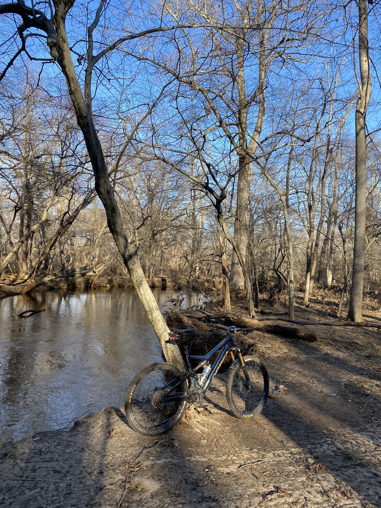 Mountain bike parked by a calm river under bare trees on a sunny day. - Dinosaurs Loop