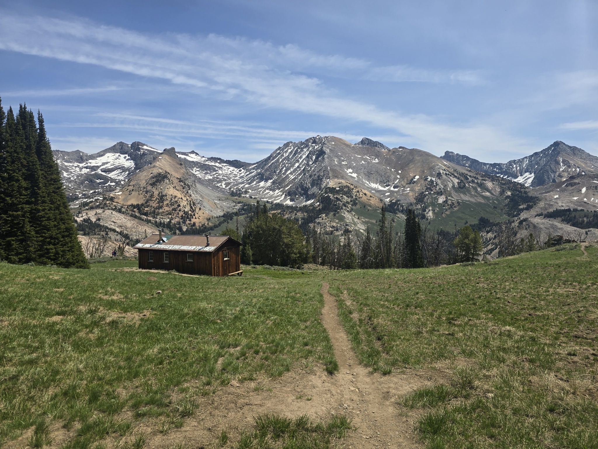 Wooden cabin in a grassy field with distant snow-capped mountains under a clear sky. - Long Gulch to Pioneer Cabin Loop