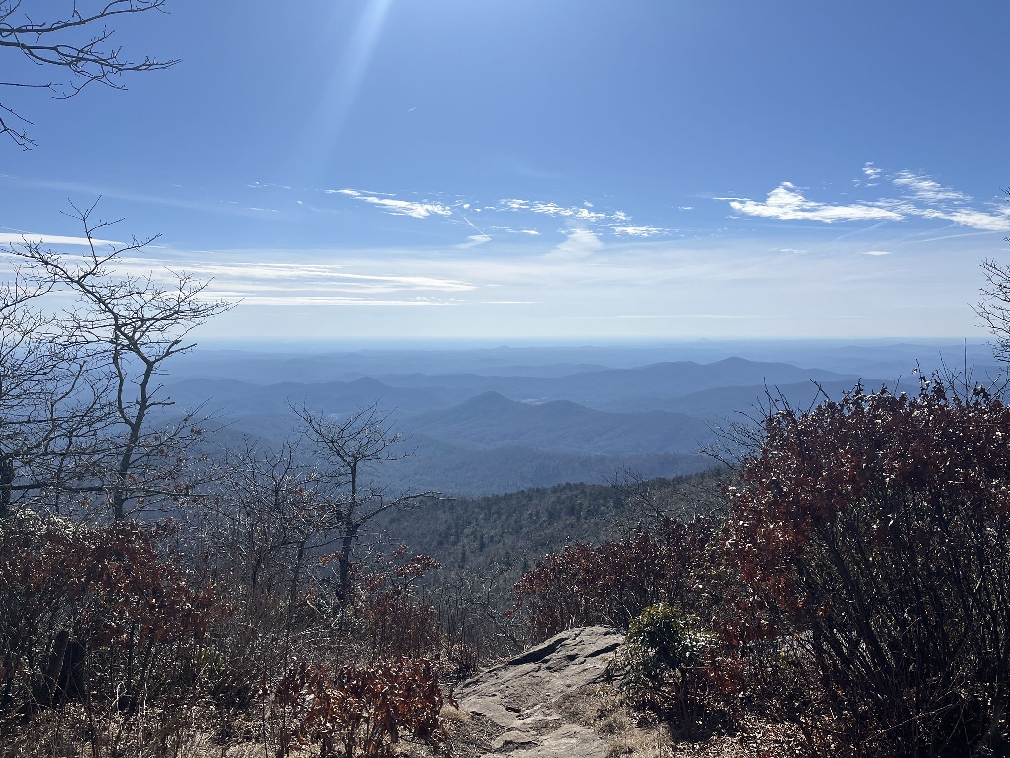 Sunny mountain vista with distant peaks and bare trees in the foreground. - Rabun Bald via Beegum Gap