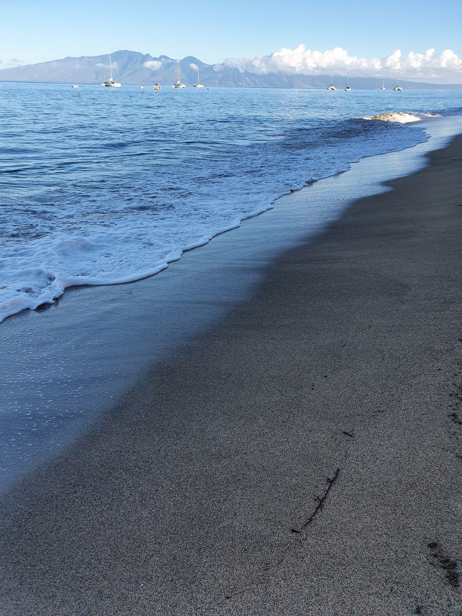 Ocean waves gently washing onto a dark sandy beach with distant mountains. - Black Rock Beach loop from Kaanapali