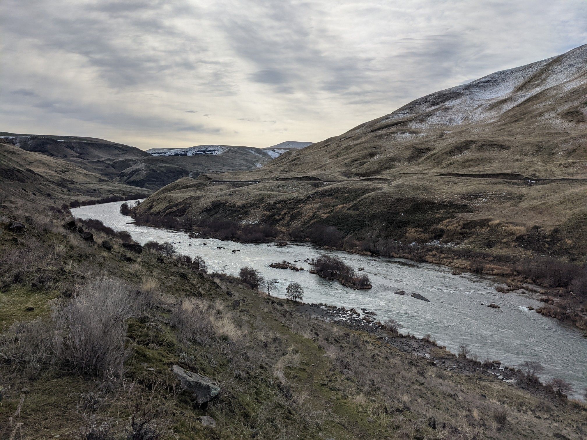 A wide river winds through a dry valley with distant snowy hills under clouds. - Ferry Springs Trail junction loop from Last Ditch Camp