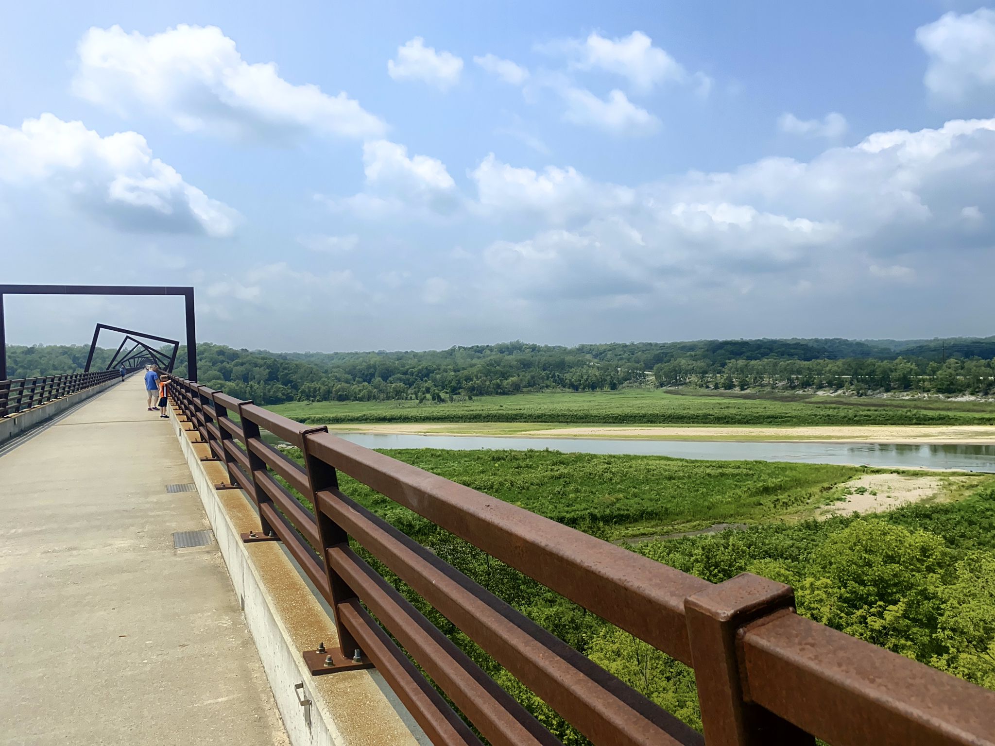 Long pedestrian bridge over a wide river, green landscape, cloudy sky. - High Trestle Trail