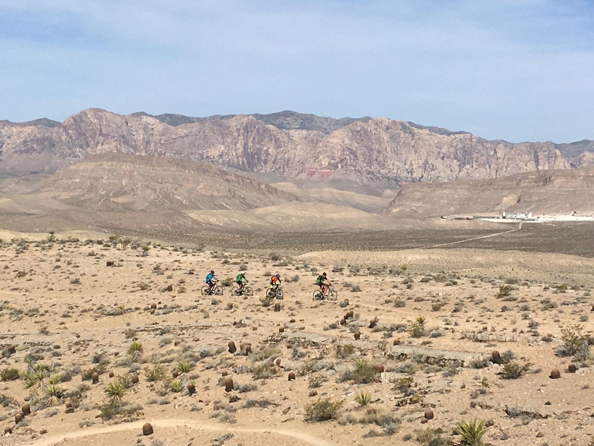 Four mountain bikers riding across a wide desert landscape. - Bears Best Trailhead – Downtown Summerlin loop from Summerlin South