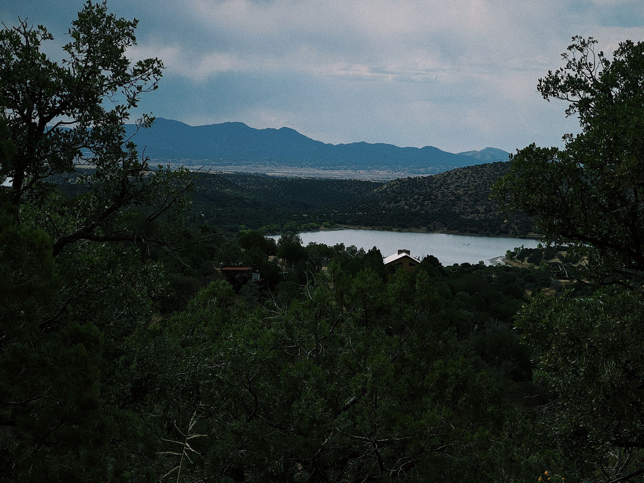 Overcast view of a lake nestled among trees with distant mountains. - Patagonia – Harshaw Road Trailhead loop from Patagonia