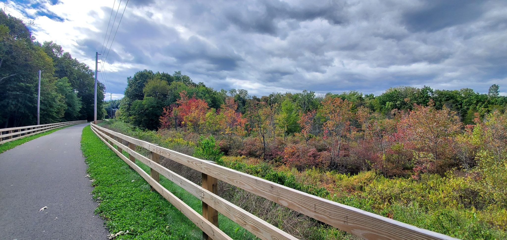 Paved path with a wooden fence alongside colorful autumn foliage. - Albany-Hudson Electric Trail – Nassau Lake loop from Albany-Rensselaer