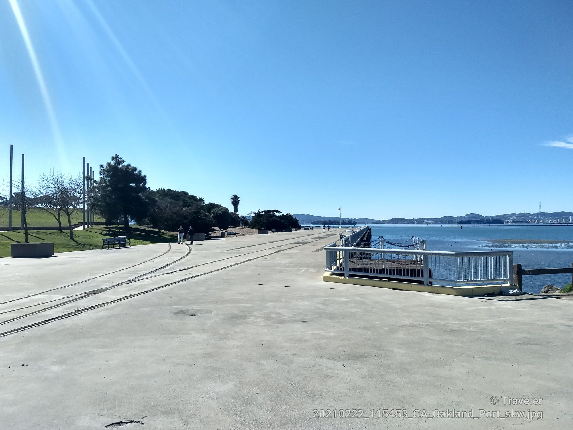 Wide paved area beside calm water, with a small dock and bright sun. - San Francisco Bay Trail: Middle Harbor Shoreline Park
