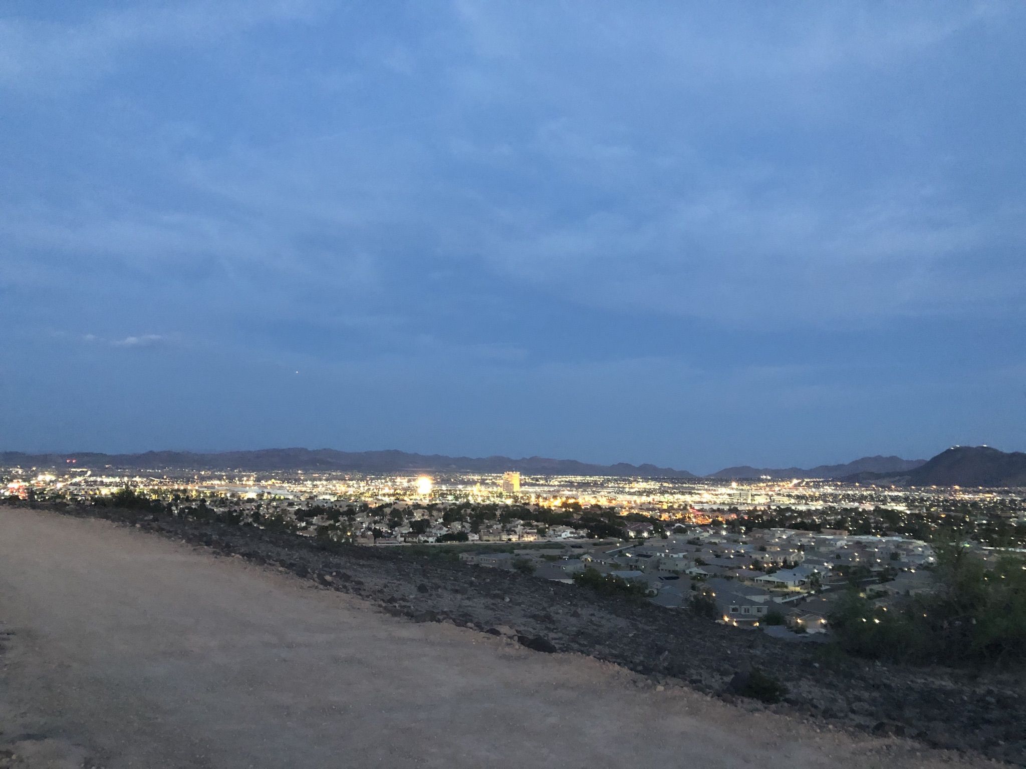 City lights glow at dusk from a dirt path overlooking a vast urban landscape. - Whitney Mesa Hiking Trail