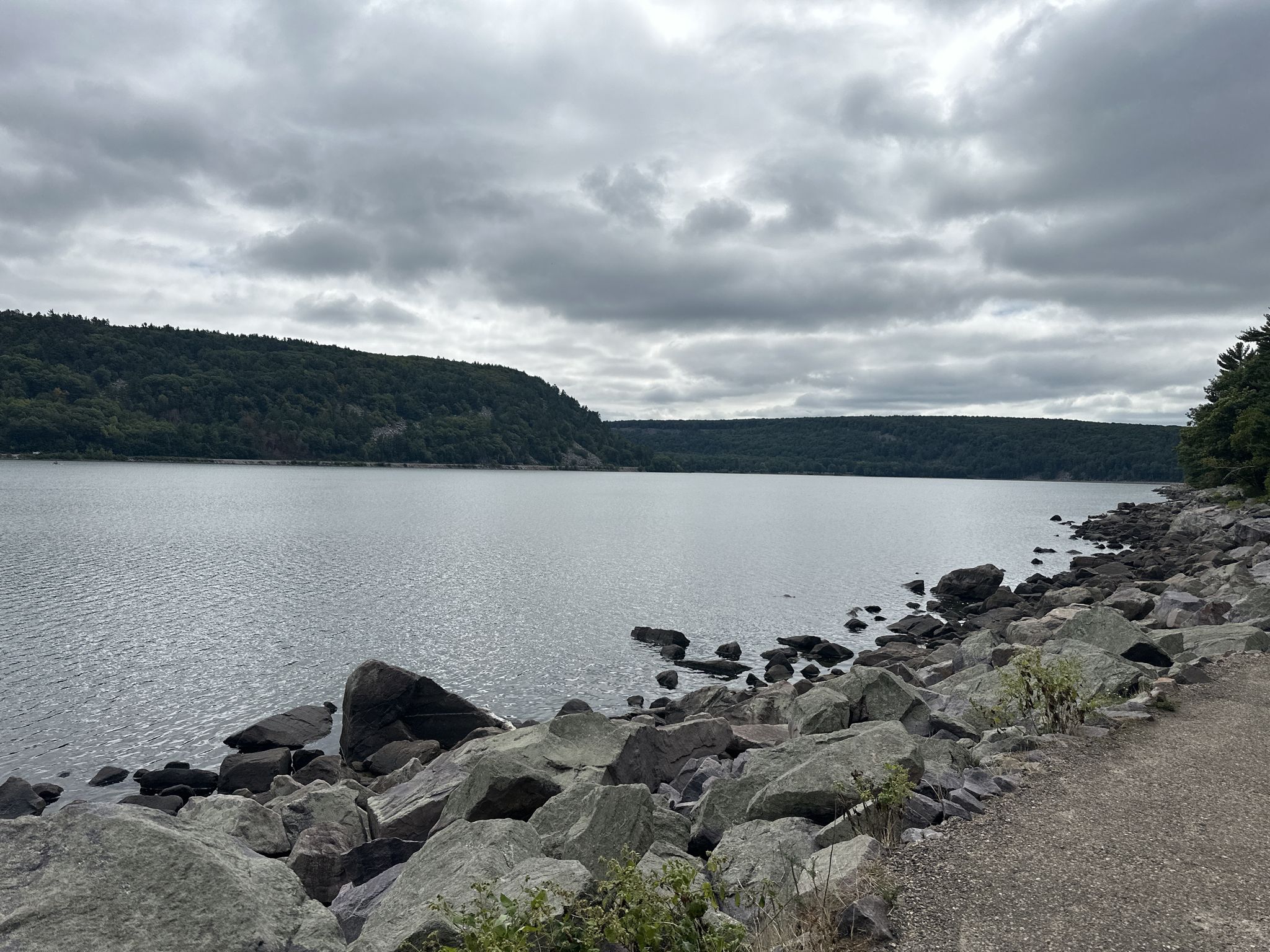 Overcast view of a lake with rocky shore and forested hills. - Tumbled Rocks Trail
