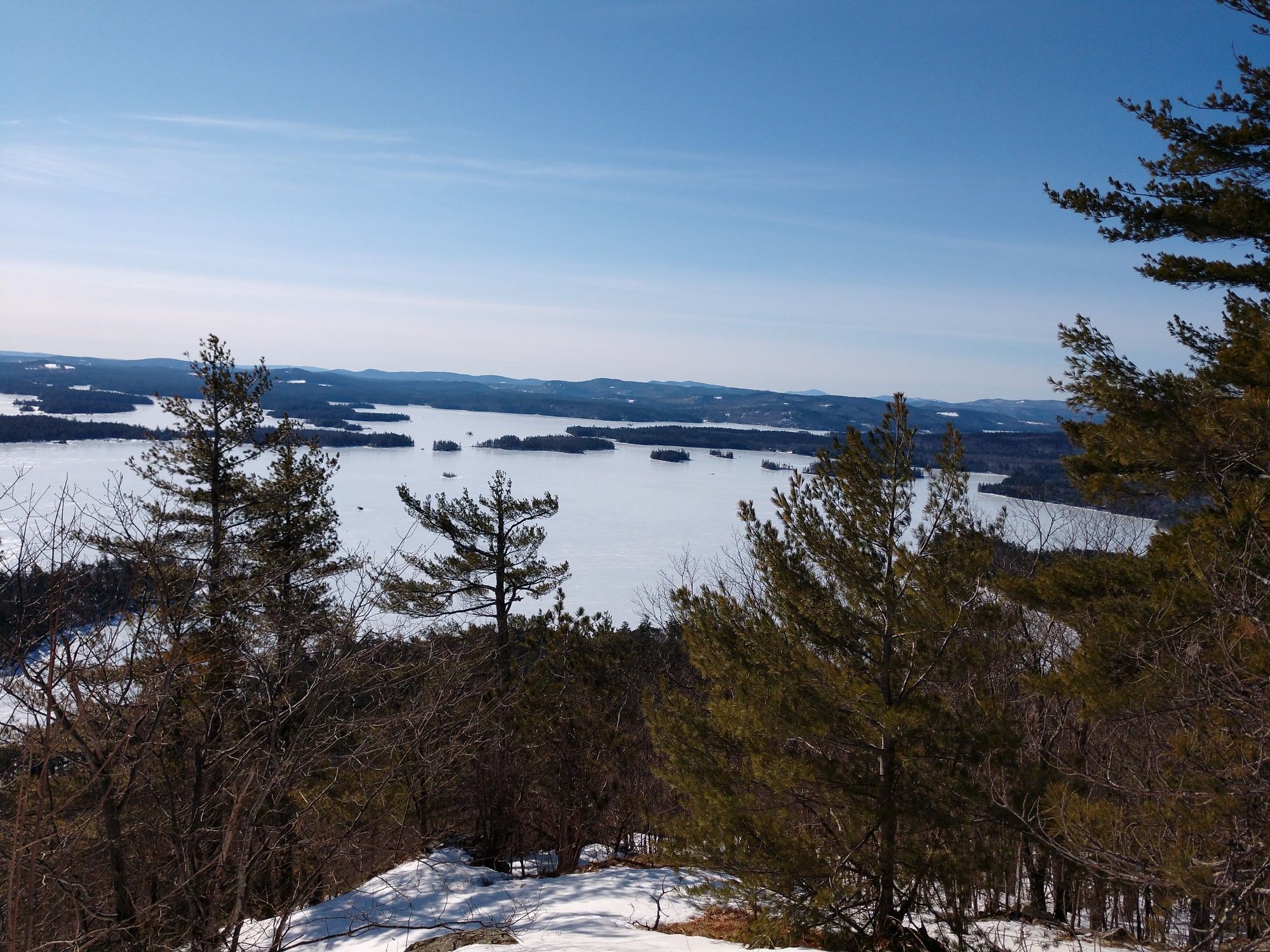 Pine trees frame a vast frozen lake under a clear blue sky. - East Rattlesnake Trail