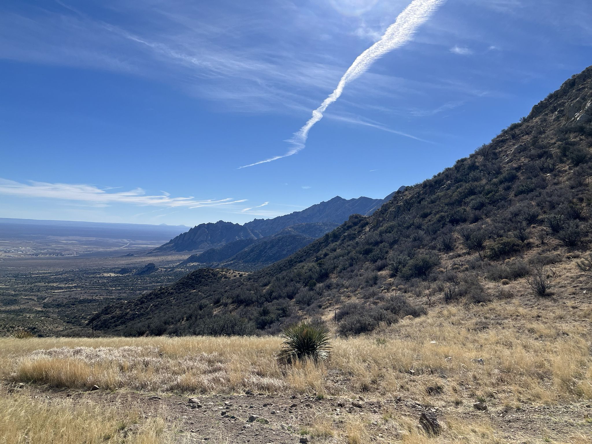 Expansive mountain landscape with a valley, dry grass, and a contrail in the sky. - Baylor Canyon Pass Trail