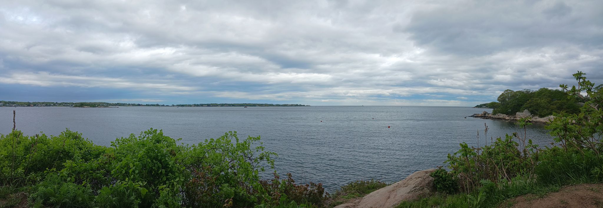 Panoramic view of a wide bay with green foliage under a cloudy sky. - Stage Fort Trail