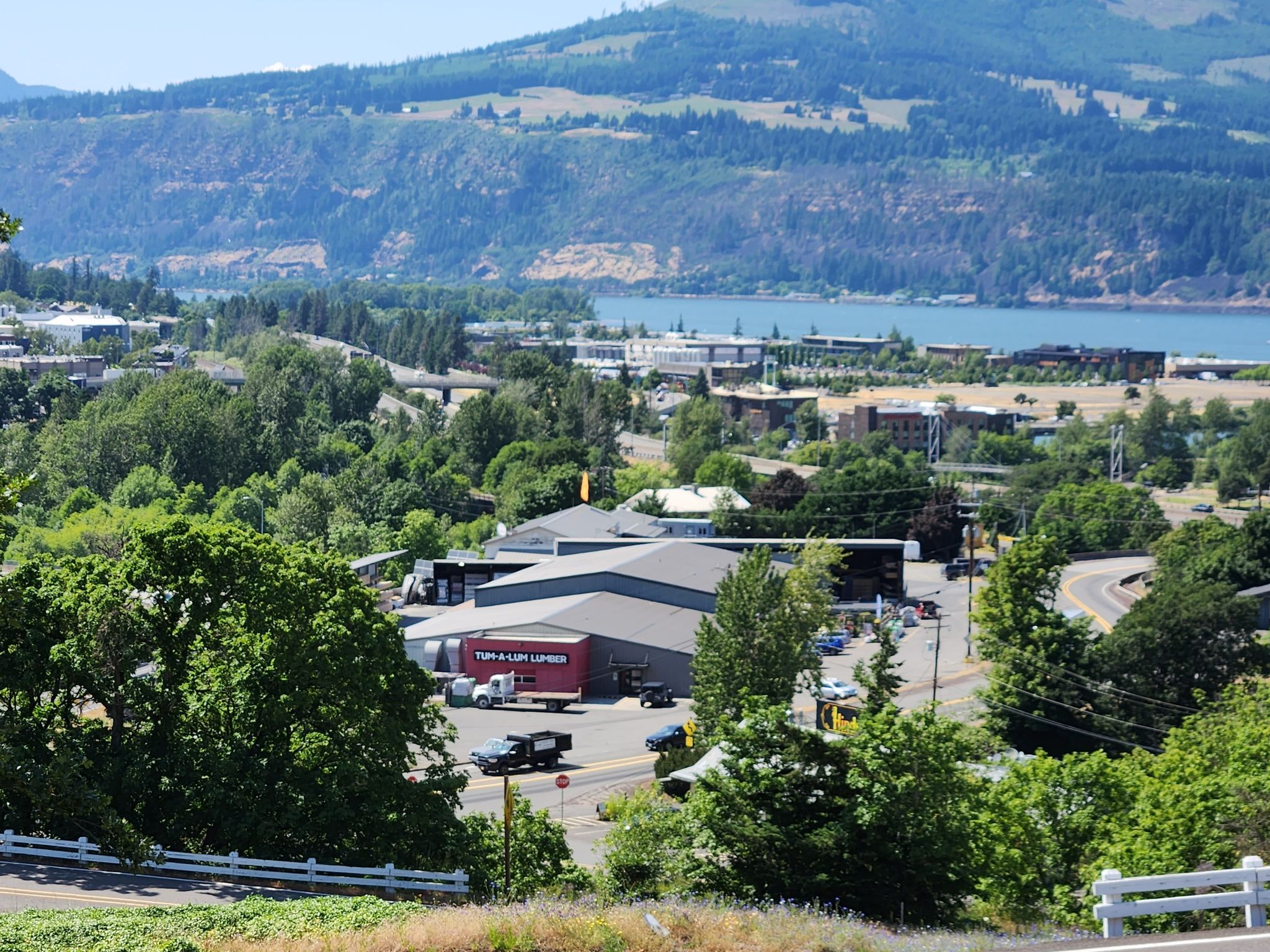 Town buildings and roads by a wide river, green hills, sunny day. - Hood River to The George White House loop